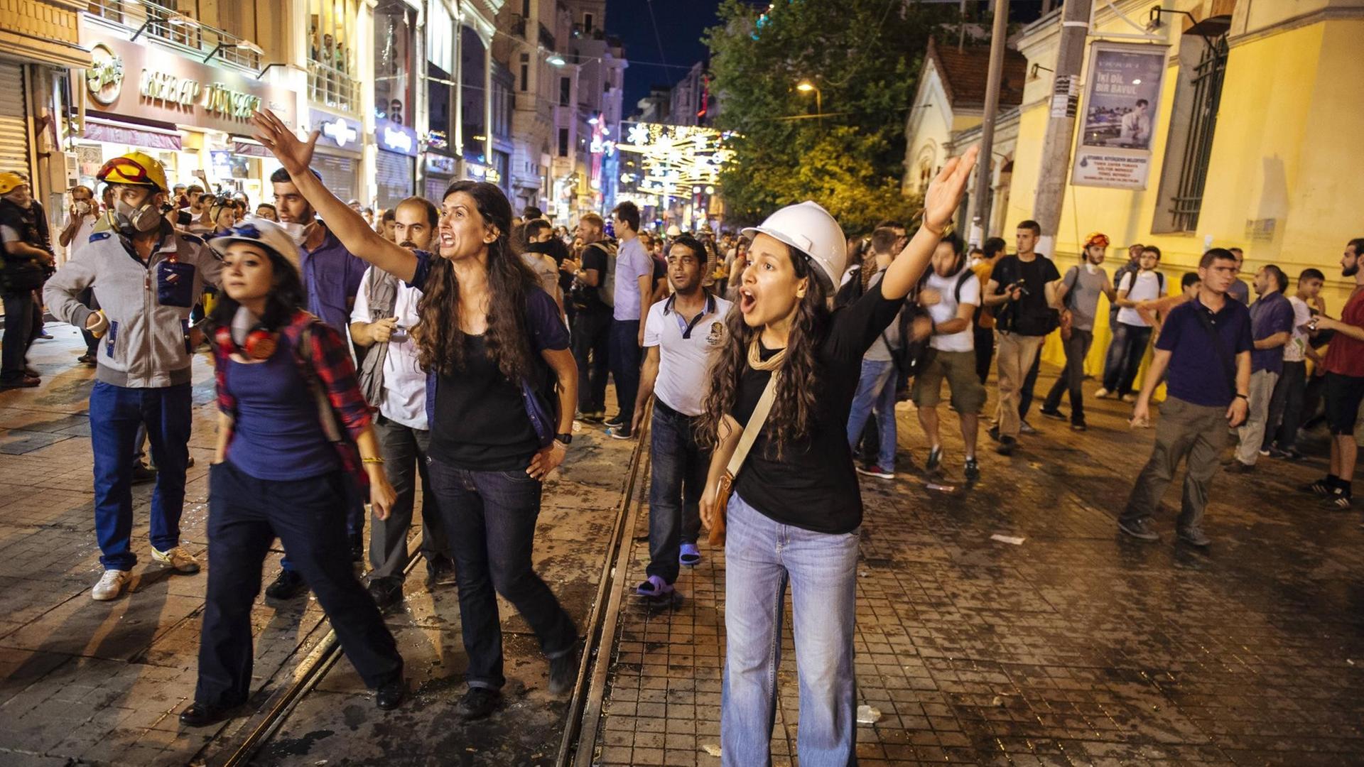 Junge Frauen mit Bauhelmen protestieren bei einer abendlichen Demonstration. Junge Frauen mit Bauhelmen protestieren bei einer abendlichen Demonstration.