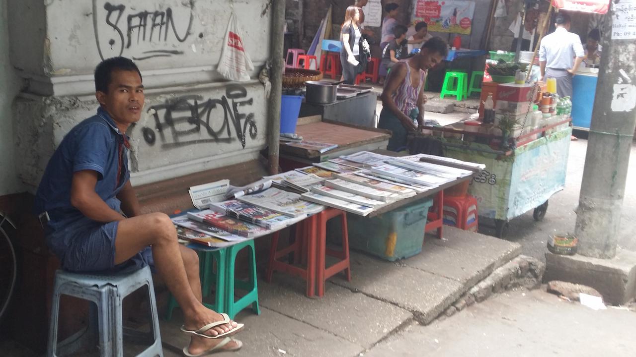 Myanmar - Presse: Ein Mann sitzt auf der Straße in Yangon und verkauft Zeitungen an einem Stand Myanmar - Presse: Ein Mann sitzt auf der Straße in Yangon und verkauft Zeitungen an einem Stand
