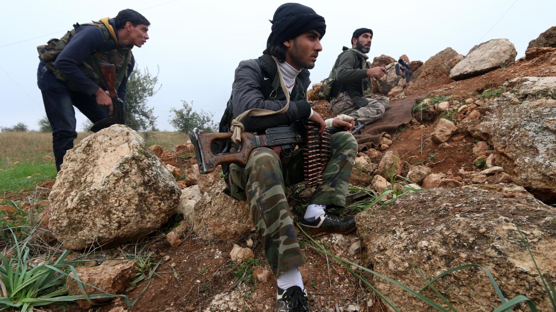 Drei bewaffnete Al-Nusra-Kämpfer kauern an einem steinigen Hügel. Drei bewaffnete Al-Nusra-Kämpfer kauern an einem steinigen Hügel.