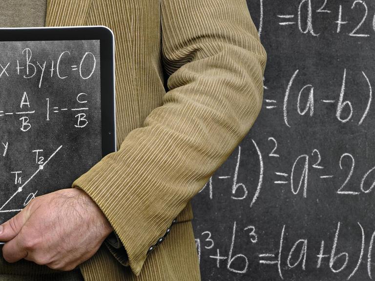 Lehrer hält einen Tablet-Computer vor einer Tafel, auf dem eine Tafel abgebildet ist.