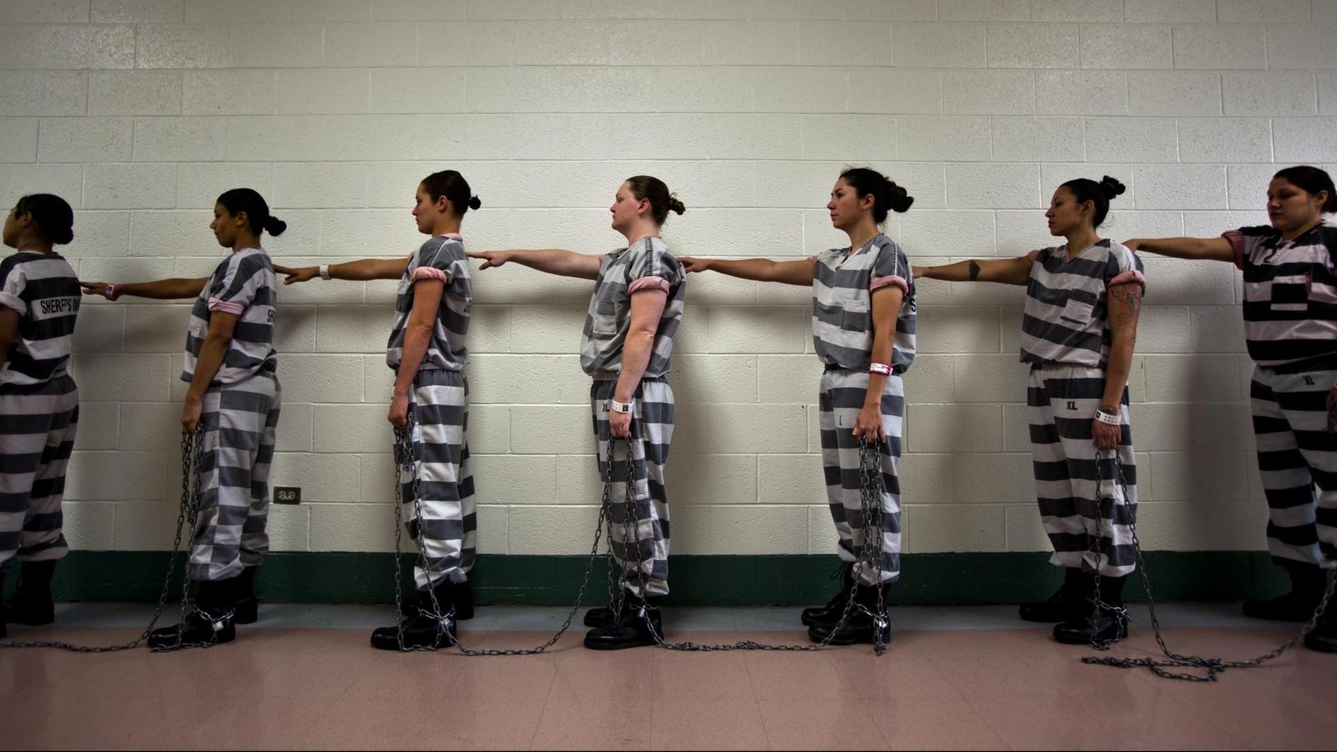Frauen stehen in Häftlingskleidung im Estrella- Gefängnis in Phoenix in einer Reihe. Jede hat ihren rechte Hand auf die Schulter der Frau vor ihr gelegt.