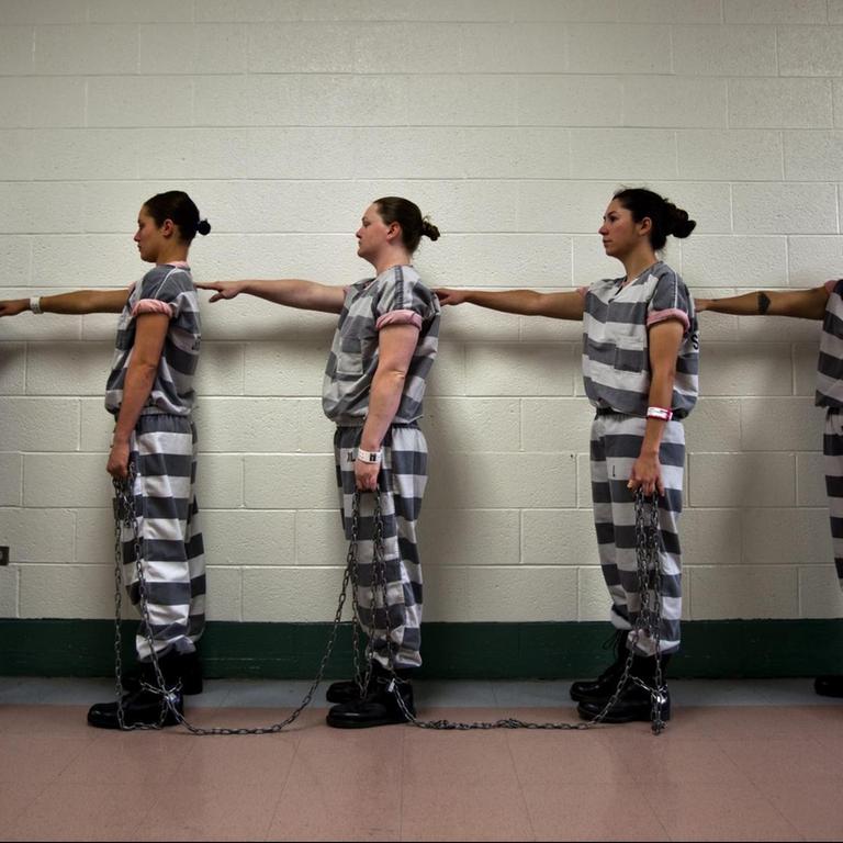 Frauen stehen in Häftlingskleidung im Estrella- Gefängnis in Phoenix in einer Reihe. Jede hat ihren rechte Hand auf die Schulter der Frau vor ihr gelegt.