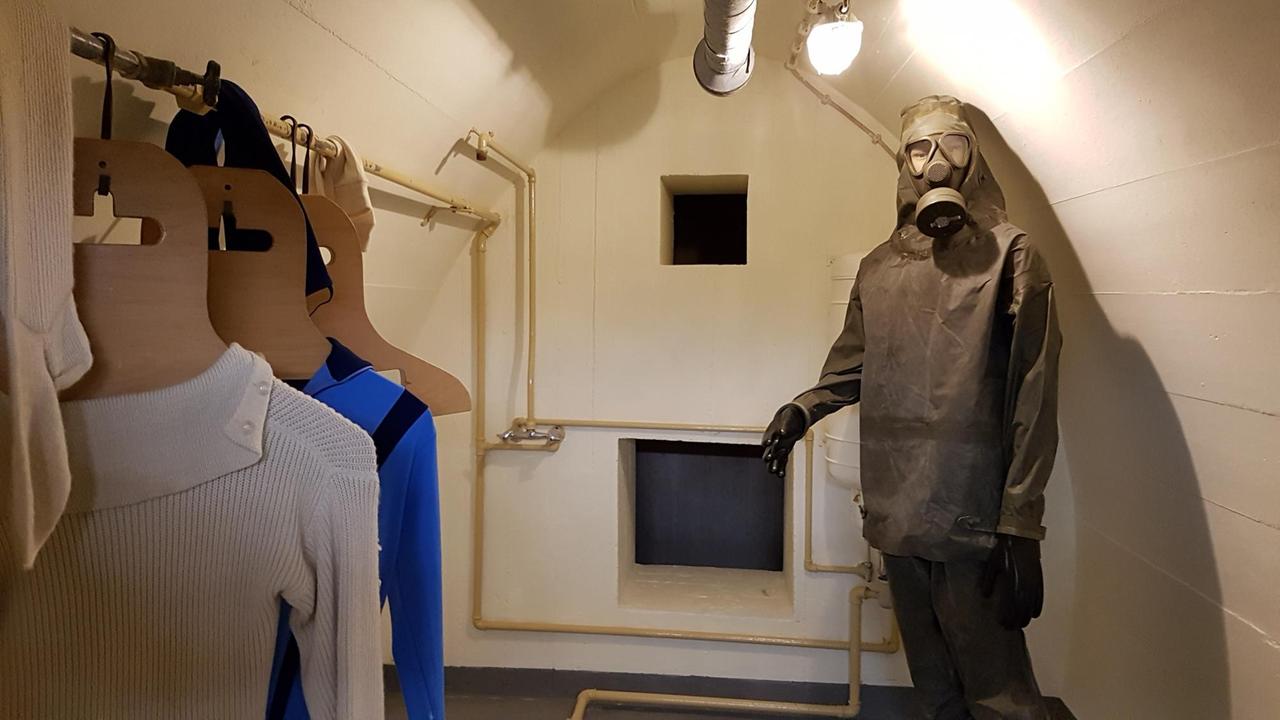 Unter einer gewölbten Betondecke steht in der Ecke eines kleinen Raumes ein Strahlenschutzanzug Unter einer gewölbten Betondecke steht in der Ecke eines kleinen Raumes ein Strahlenschutzanzug