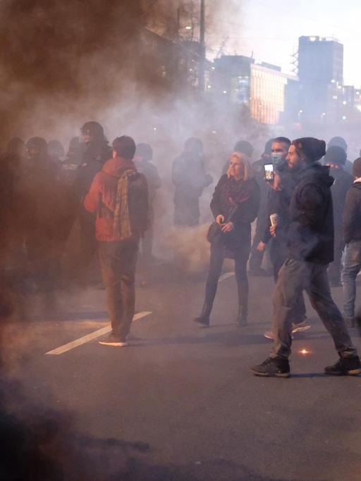Bei einer Demonstration der Stuttgarter Initiative „Querdenken“ kommt es zu Auseinandersetzungen zwischen Teilnehmern und der Polizei. Auf der Straße stehen Demonstrierende im Rauch.