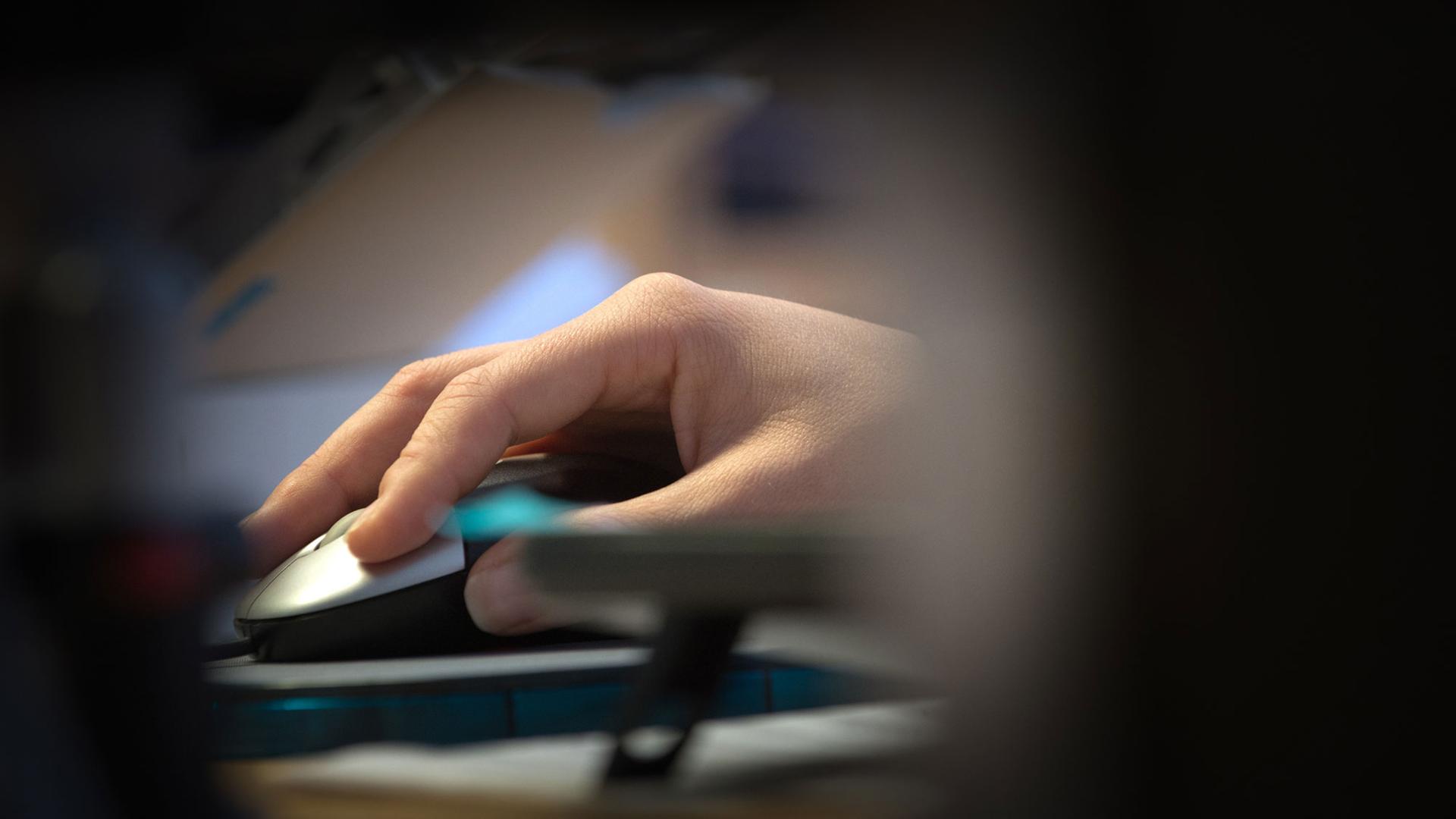 Eine Hand mit Computermaus wird durch eine Lücke in der Büroeinrichtung hindurch beobachtet. Eine Hand mit Computermaus wird durch eine Lücke in der Büroeinrichtung hindurch beobachtet.
