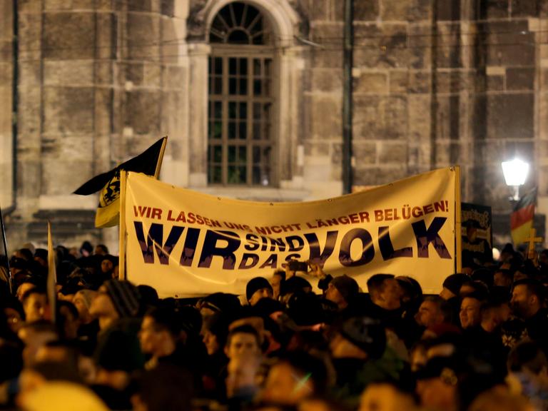 Pegida-Demonstranten halten ein Tranparent hoch, auf dem "Wir sind das Volk" steht.