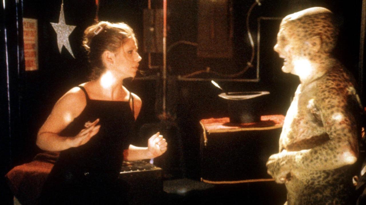 Die Schauspielerin Sarah Michelle Gellar, blond in einem schwarzen Top (links im Bild), steht kampfbereit einem Monster gegenüber, dargestellt von einem Mann in einem Ganzkörperanzug mit gefleckter Amphibienhaut.