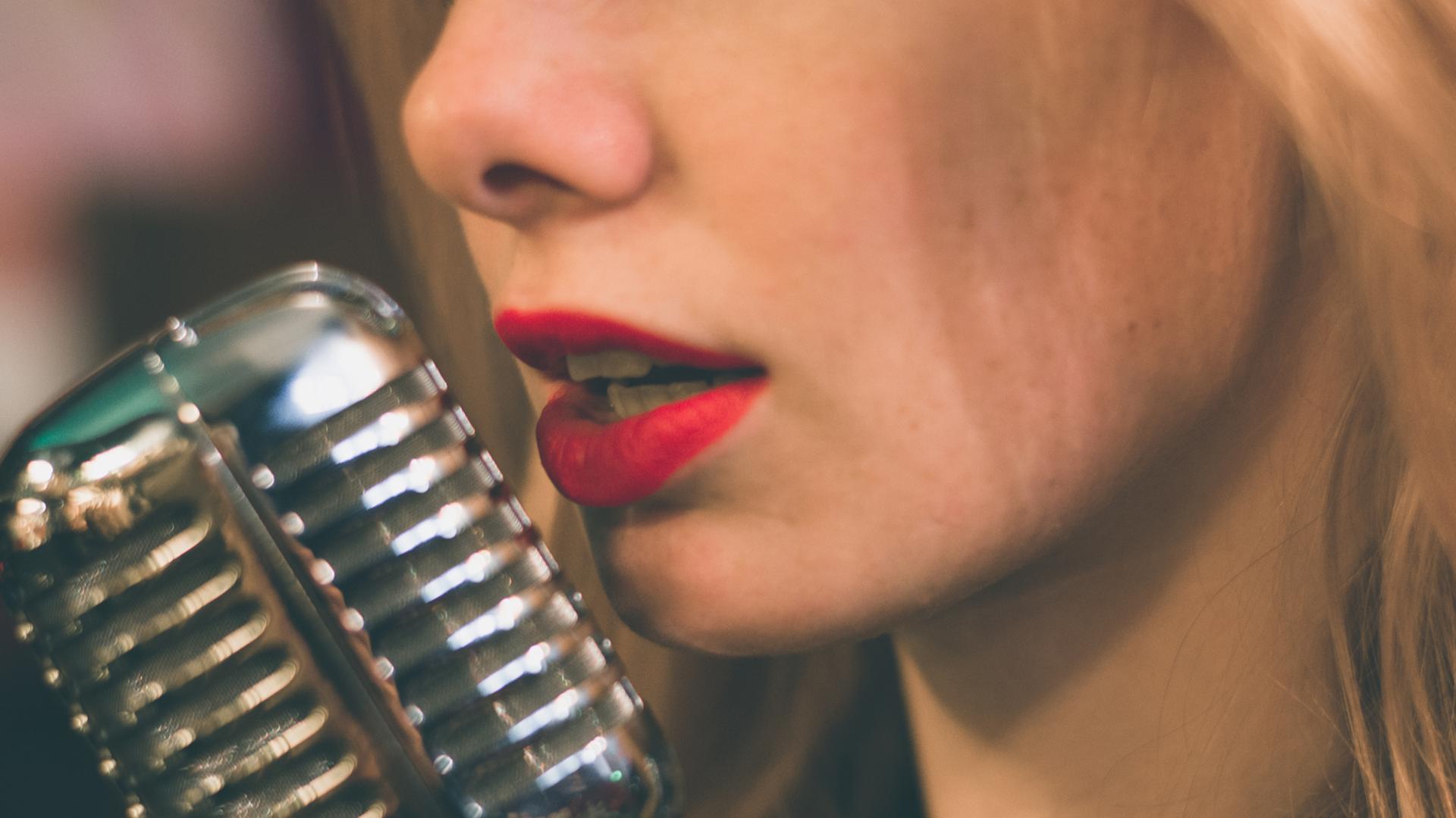 Die roten Lippen einer Sängerin vor einem Studiomikrophon Die roten Lippen einer Sängerin vor einem Studiomikrophon