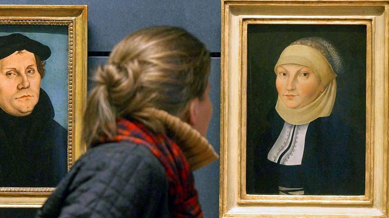 Zwei Cranach-Gemälde zeigen die Portraits von Martin Luther und seiner Frau Katharina von Bora in einer Ausstellung des Lutherhauses in Wittenberg. Der Blick einer Besucherin richtet sich auf das Abbild von Katharina von Bora.