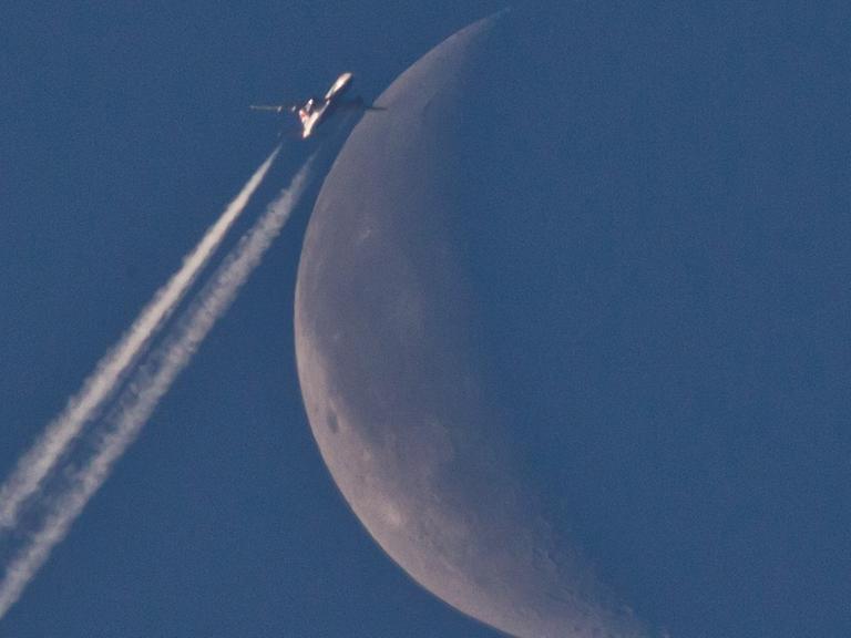 Ein Flugzeug fliegt über Nürnberg (Bayern) scheinbar am Mond vorbei.
