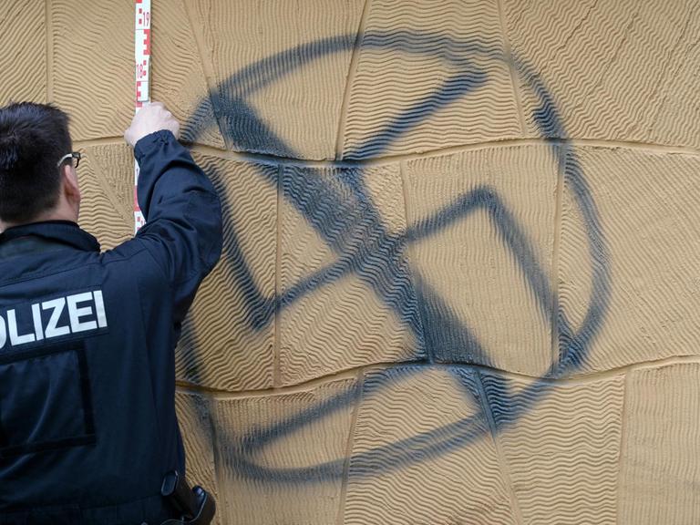 Ein Polizist sichert am 26.4.2016 an der Fassade eines Wohnhauses in Potsdam Spuren an einem gesprühten Hakenkreuz.