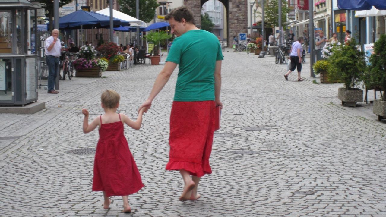 Nils Pickert läuft mit seinem Sohn die Straße entlang. Er trägt einen Rock, der Junge ein rotes Kleid.