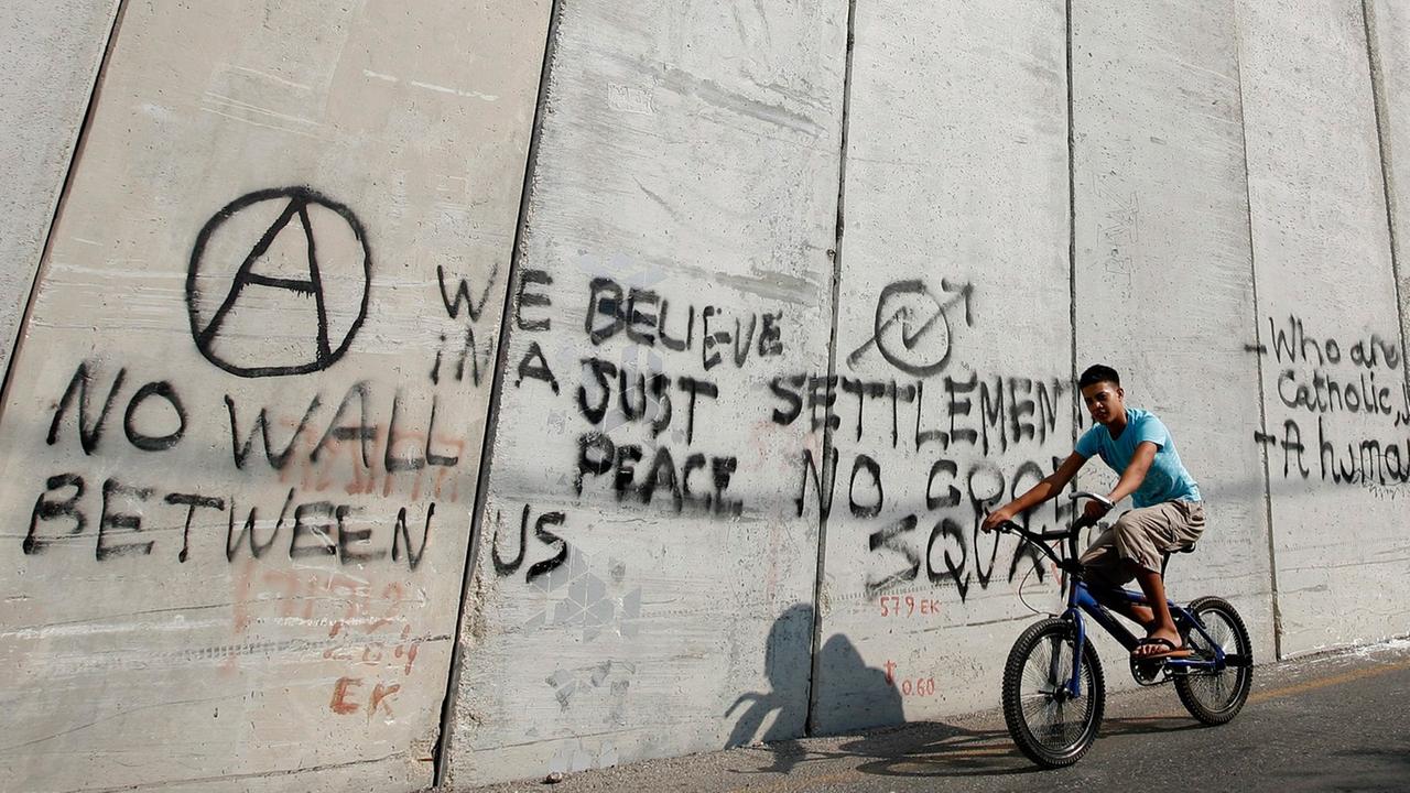 Ein arabischer Junge fährt im Osten Jerusalems auf einem Rad am Trennwall zwischen Israel und dem palästinensischen Gebiet entlang. Ein arabischer Junge fährt im Osten Jerusalems auf einem Rad am Trennwall zwischen Israel und dem palästinensischen Gebiet entlang.