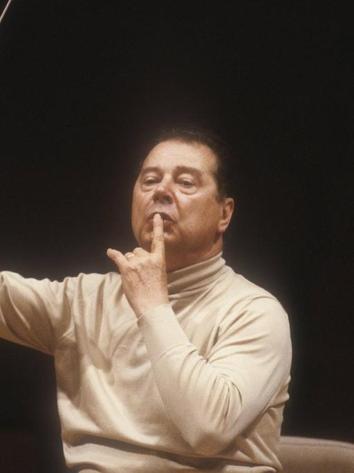 Der spanische Dirigent und Komponist Rafael Frühbeck de Burgos 1985 bei einer Probe in Rom. Er sitzt auf einem Dirigentenstuhl, dirigiert mit Taktstock und trägt einen hellen Rollkragenpullover