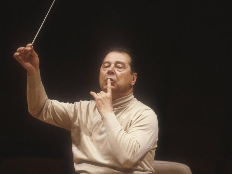 Der spanische Dirigent und Komponist Rafael Frühbeck de Burgos 1985 bei einer Probe in Rom. Er sitzt auf einem Dirigentenstuhl, dirigiert mit Taktstock und trägt einen hellen Rollkragenpullover