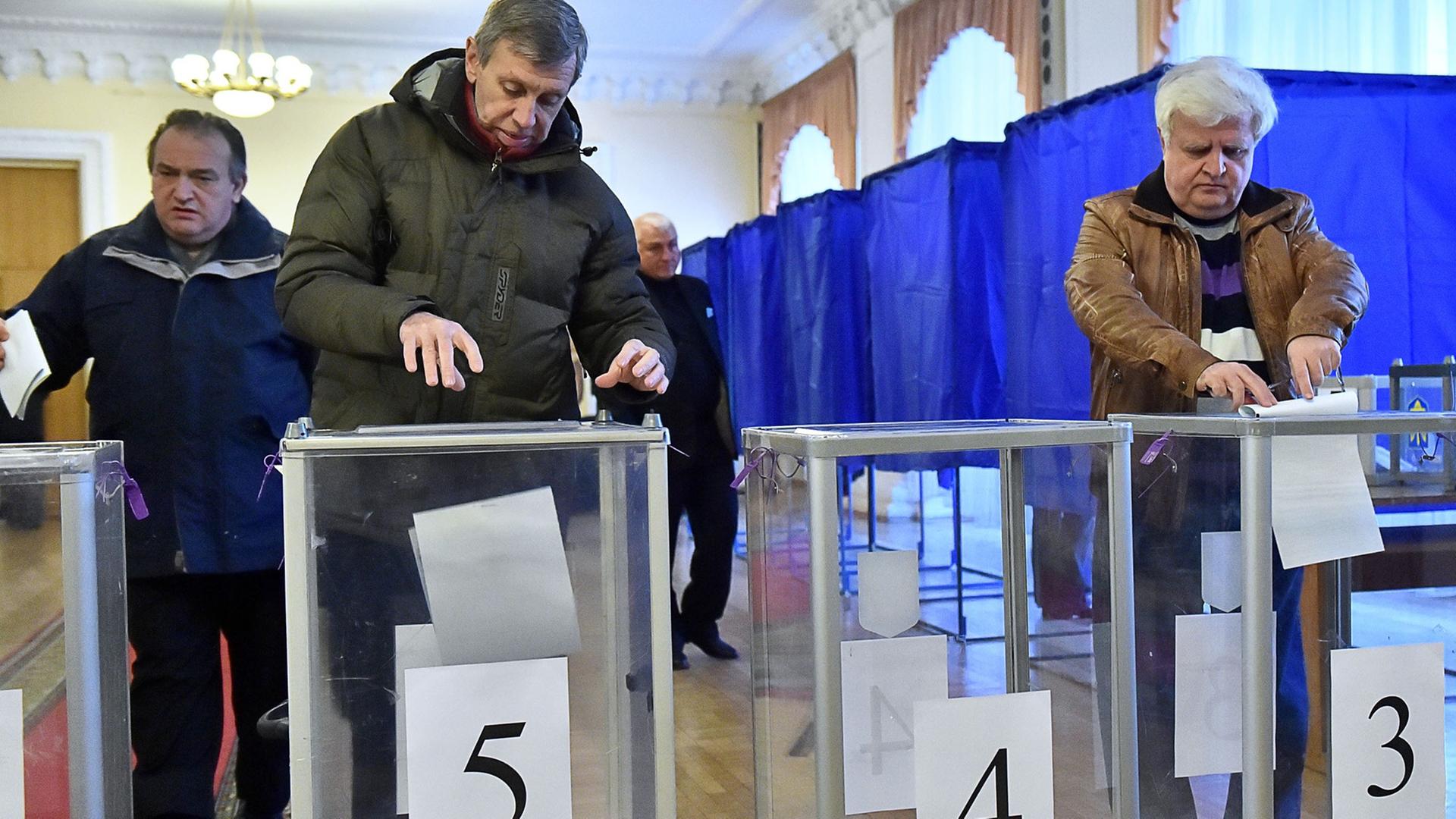 In einem Wahllokal in der ukrainischen Hauptstadt Kiew werfen zwei Männer und eine Frau ihre ausgefüllten Stimmzettel in die Wahlurnen. In einem Wahllokal in der ukrainischen Hauptstadt Kiew werfen zwei Männer und eine Frau ihre ausgefüllten Stimmzettel in die Wahlurnen.