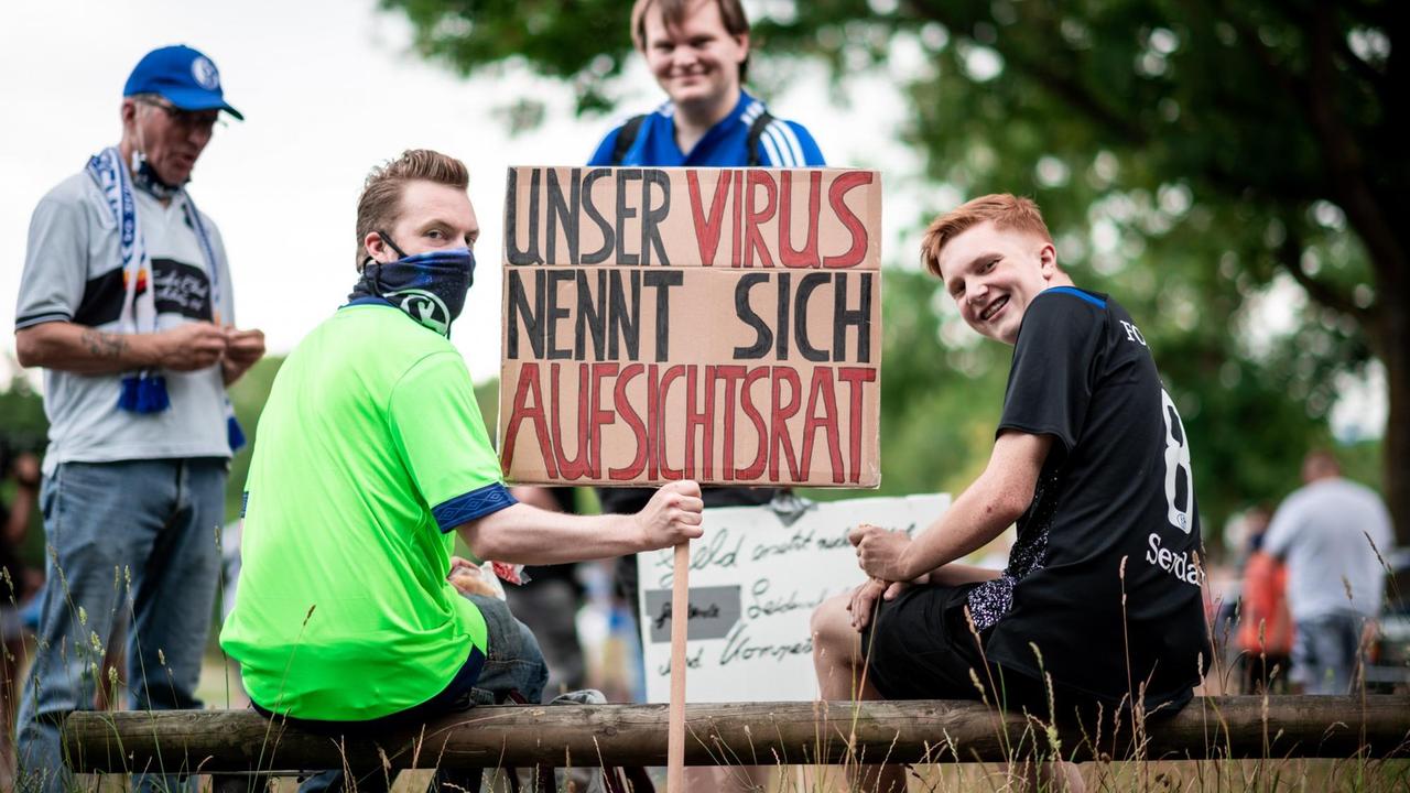 Zwei junge Männer sitzen auf einem Balken und halten ein Schild mit der Aufschrift "Unser Virus nennt sich Aufsichtsrats" in die Höhe. Dahinter weitere Demonstranten. Zwei junge Männer sitzen auf einem Balken und halten ein Schild mit der Aufschrift "Unser Virus nennt sich Aufsichtsrats" in die Höhe. Dahinter weitere Demonstranten.
