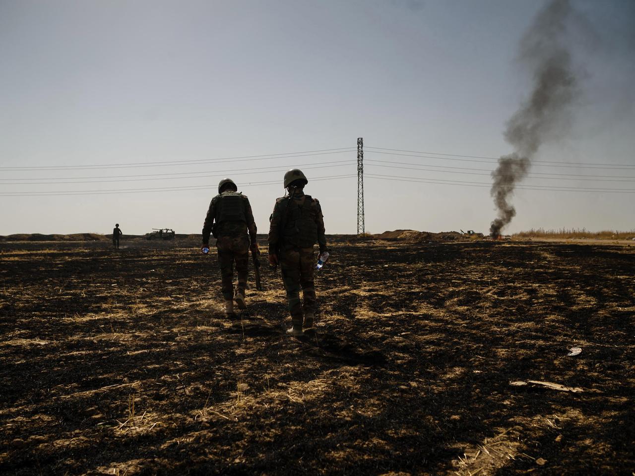 Eine karge Landschaft nahe Mossul. Zwei kurdische Soldaten laufen über ein Feld. Eine karge Landschaft nahe Mossul. Zwei kurdische Soldaten laufen über ein Feld.