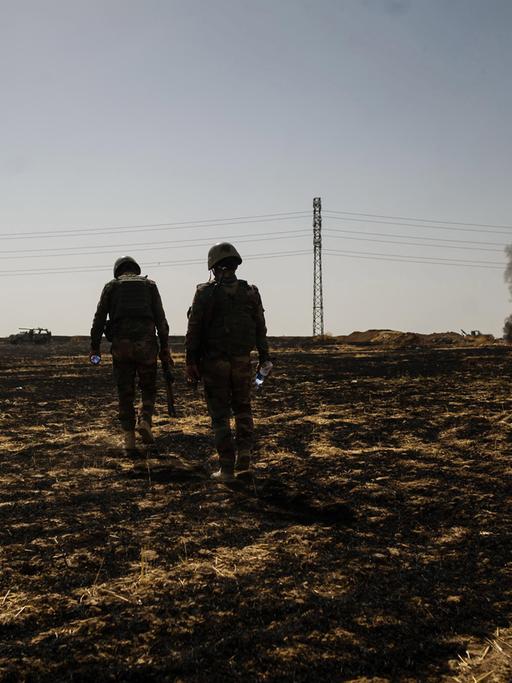 Eine karge Landschaft nahe Mossul. Zwei kurdische Soldaten laufen über ein Feld.