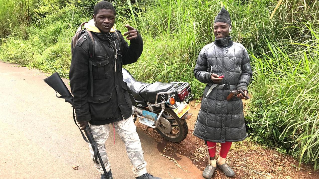 Zwei Separatisten stehen in Kamerun vor einem Motorrad, einer hält eine Waffe in der Hand