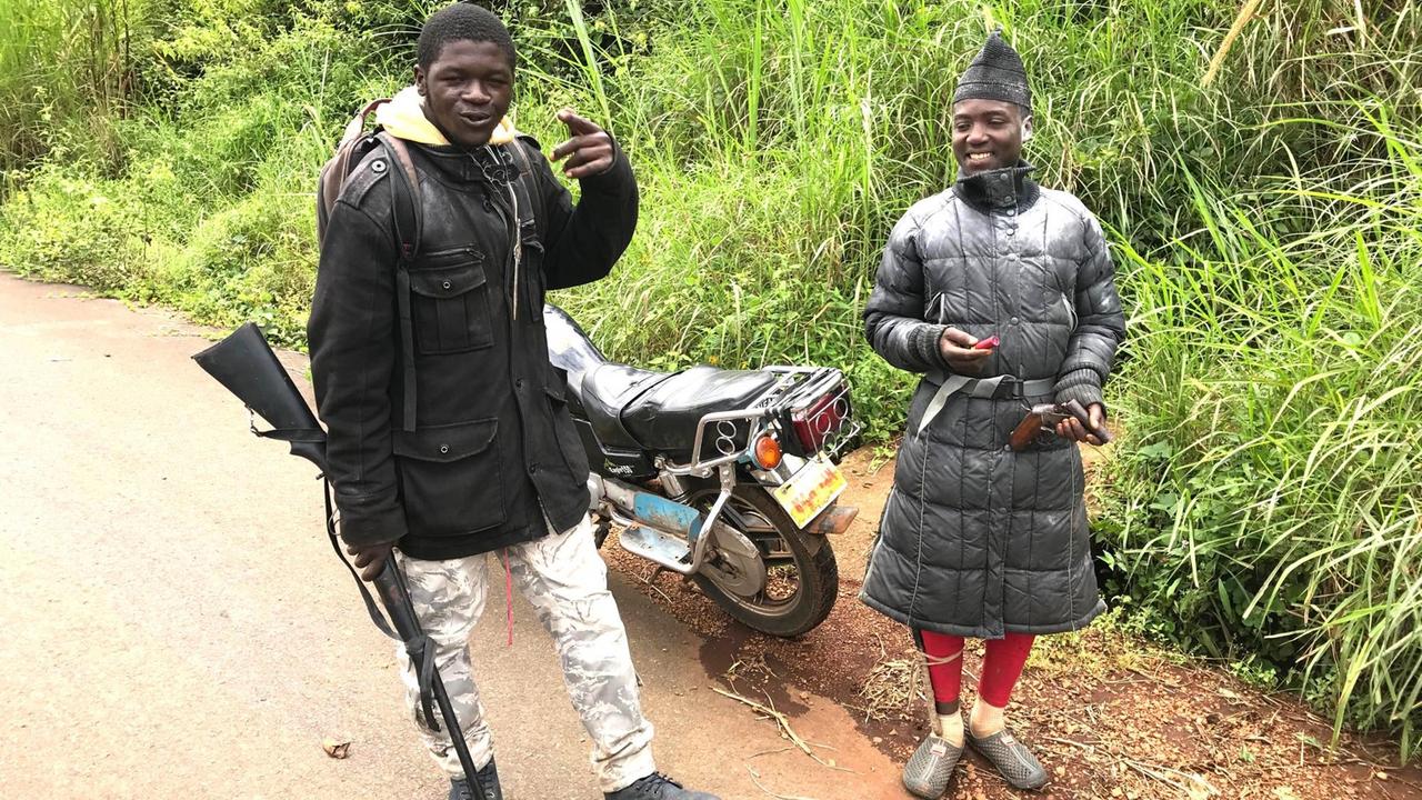 Zwei Separatisten stehen in Kamerun vor einem Motorrad, einer hält eine Waffe in der Hand Zwei Separatisten stehen in Kamerun vor einem Motorrad, einer hält eine Waffe in der Hand