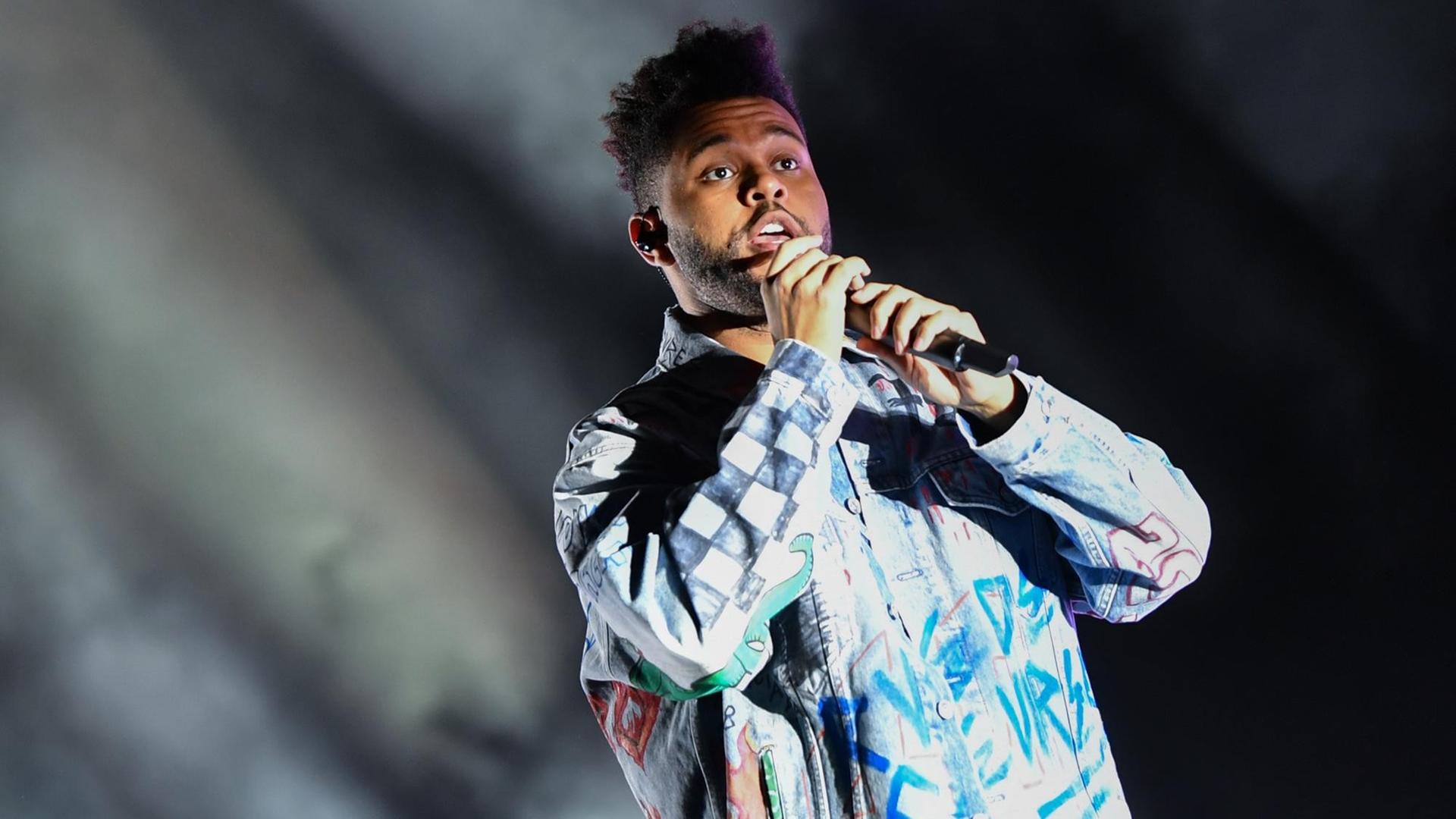 Sänger The Weeknd mit Jeansjacke und Mikrofon auf der Bühne Sänger The Weeknd mit Jeansjacke und Mikrofon auf der Bühne