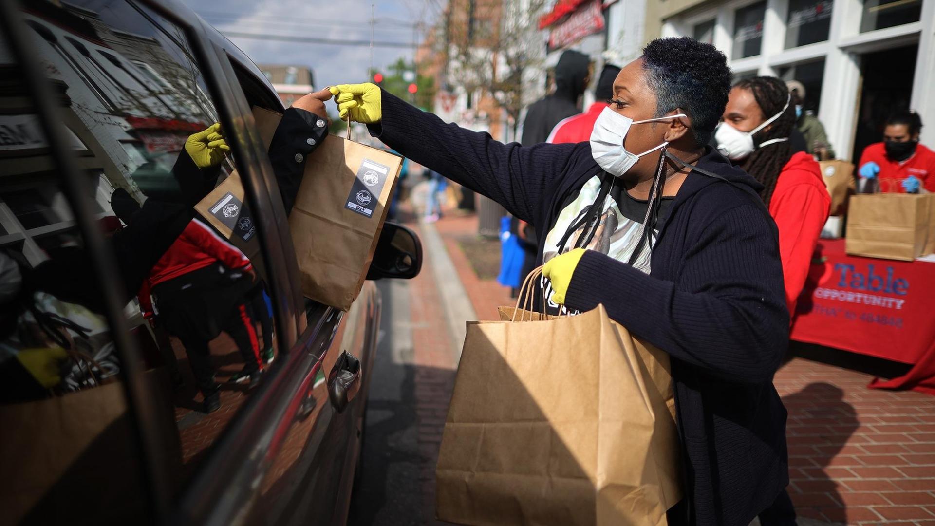 Eine Frau mit Mundschutz reicht Essen in Papiertüten in ein Auto.