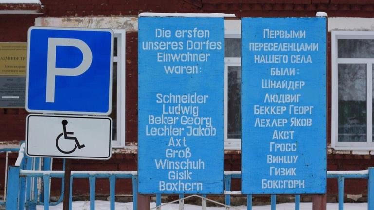 Ein Schild auf Deutsch und auf Russisch mit den Namen der ersten Einwohner steht im Dorf Aleksandrowka Ein Schild auf Deutsch und auf Russisch mit den Namen der ersten Einwohner steht im Dorf Aleksandrowka