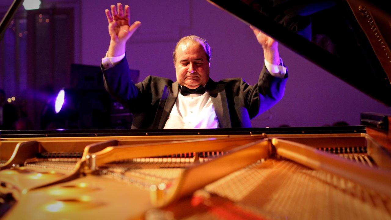 Ein Pianist, an der Tastatur sitzend, erhebt seine massiven Hände hoch über den Kopf nach einem finalen Schlussklang.