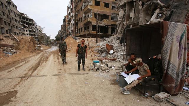 Zwei Männer stehen auf einer Straße umringt von zerstörten Gebäuden