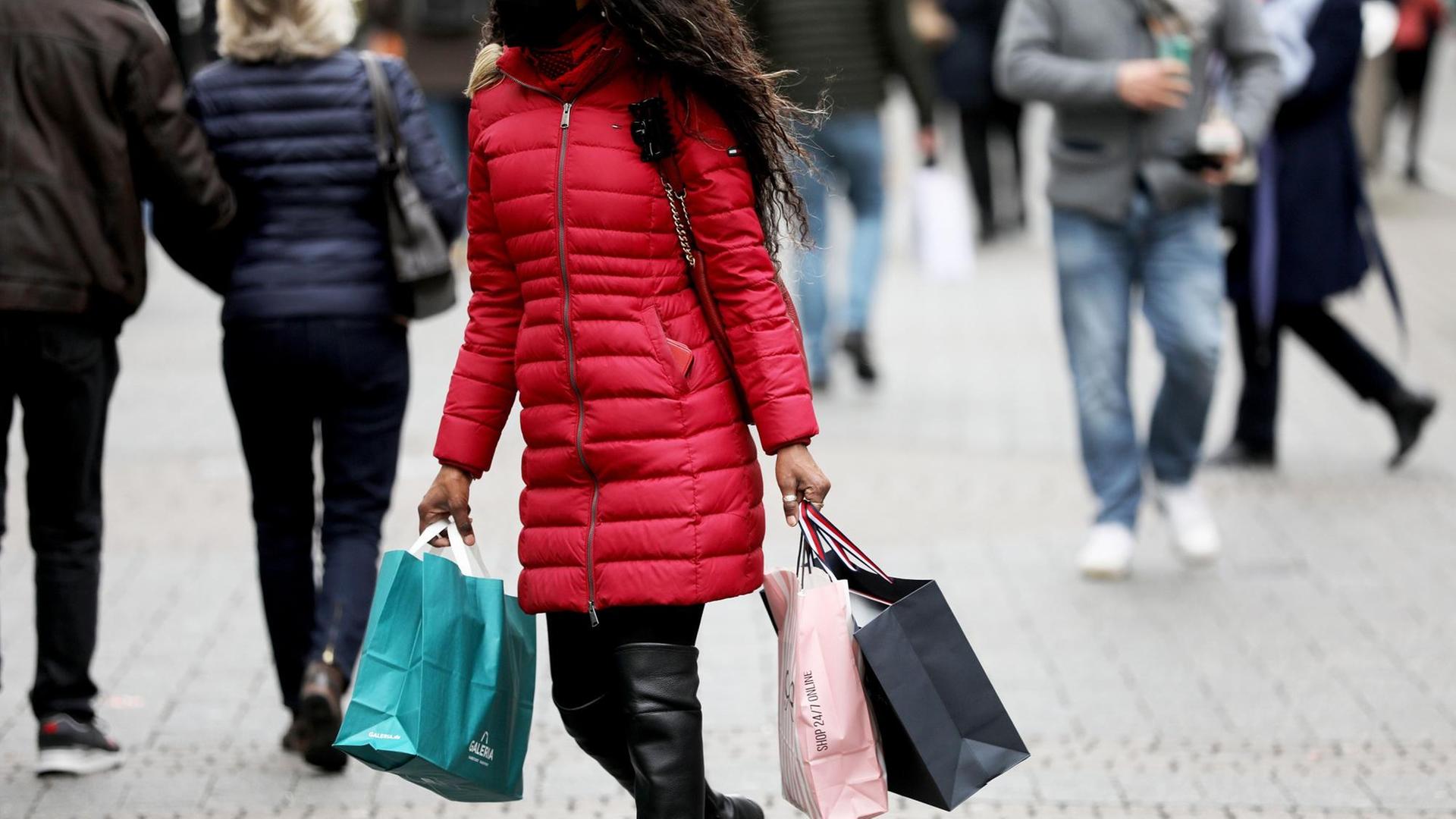 Eine Frau geht mit Einkaufstaschen durch die Kölner Fußgängerzone in der Schildergasse
