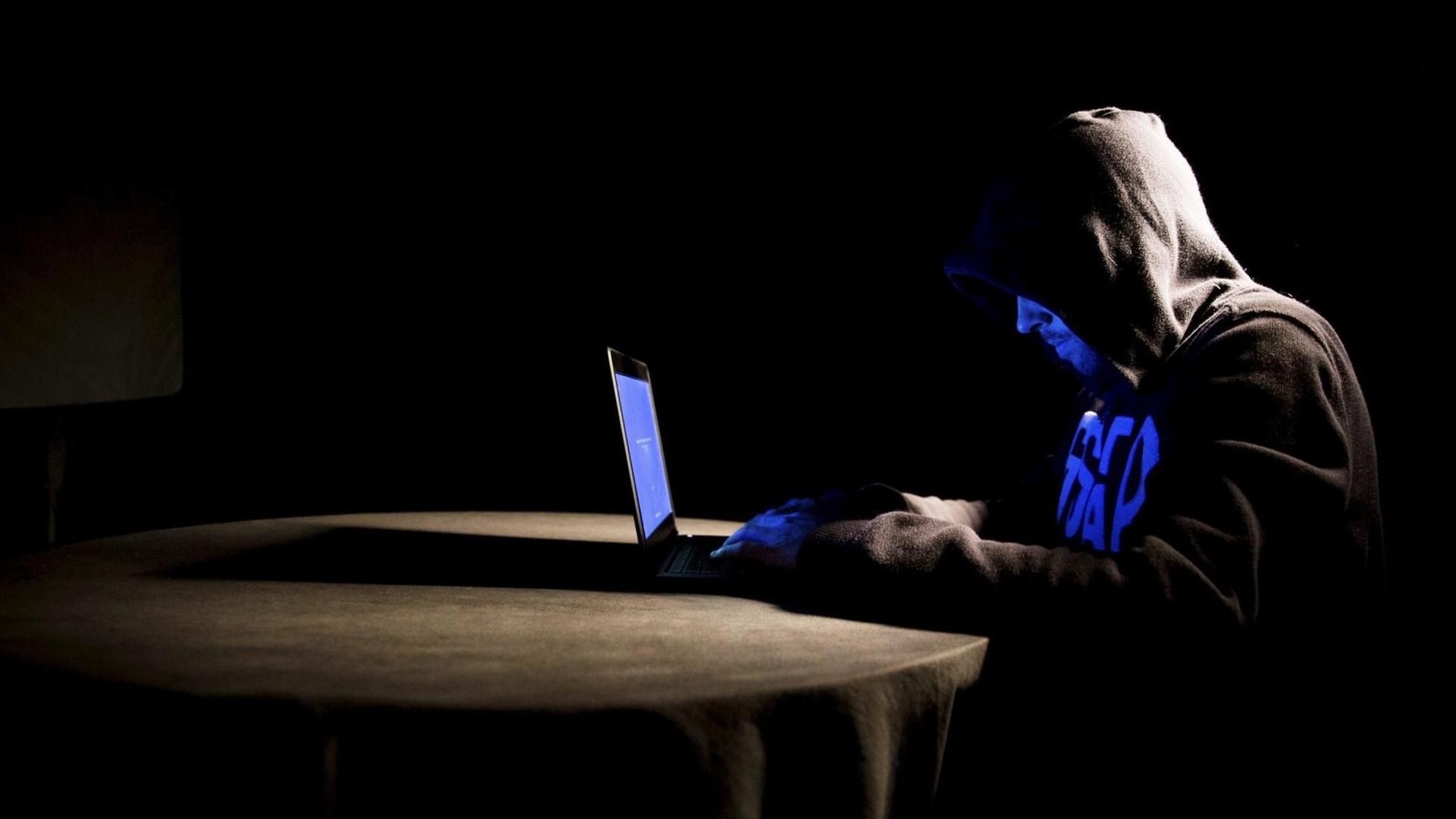 Ein Hacker mit Kapuzenpullover arbeitet an seinem Laptop Ein Hacker mit Kapuzenpullover arbeitet an seinem Laptop