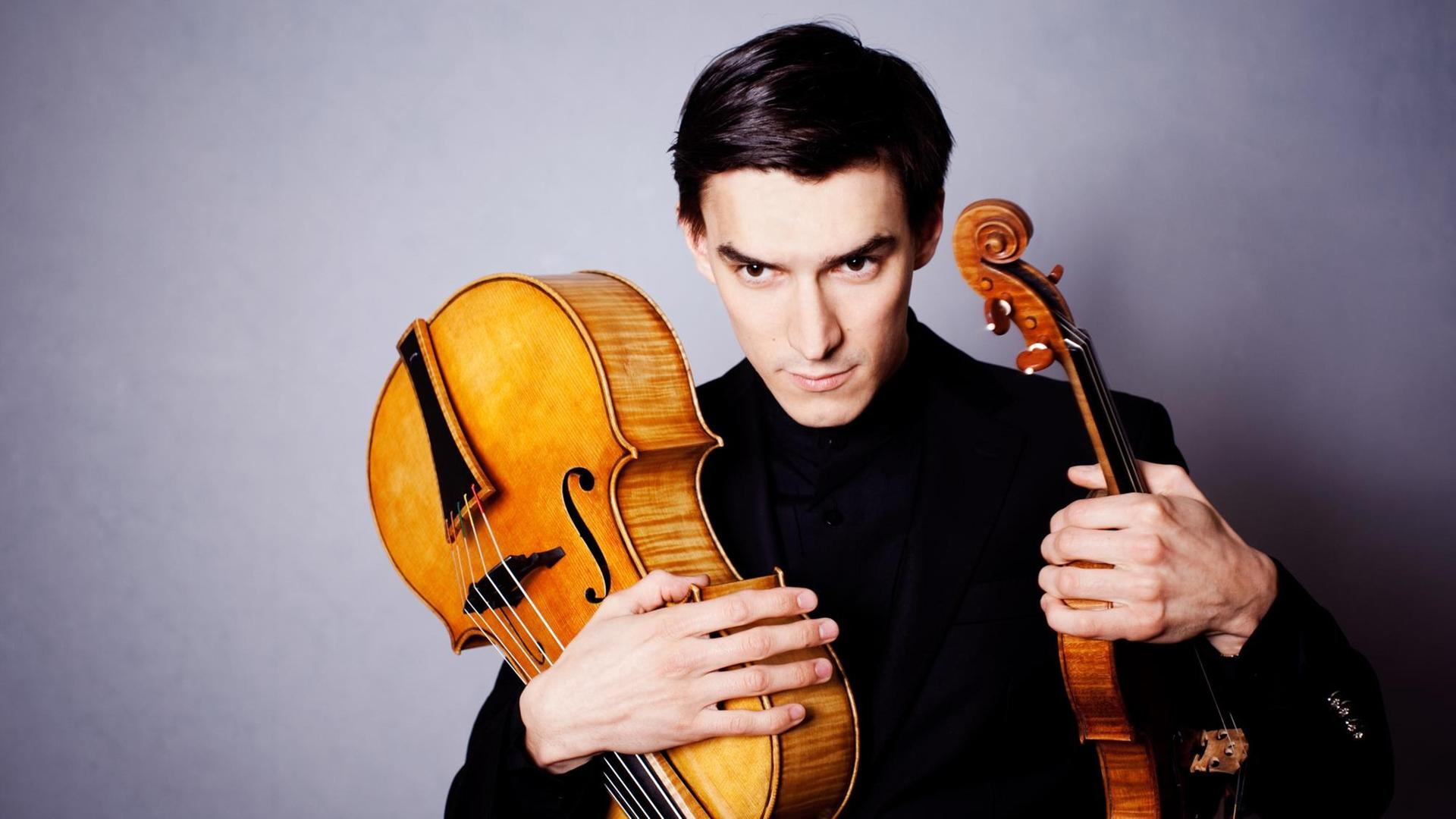Der Geiger Sergey Malov hält in der einen Hand eine Violine und in der anderen ein Violoncello da spalla Der Geiger Sergey Malov hält in der einen Hand eine Violine und in der anderen ein Violoncello da spalla