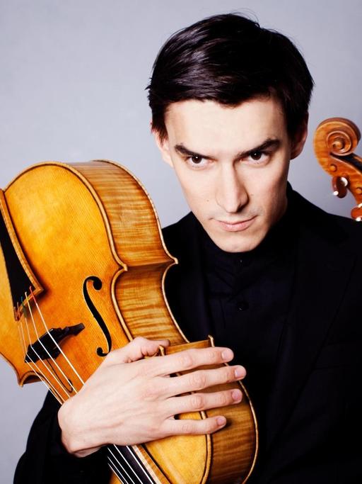 Der Geiger Sergey Malov hält in der einen Hand eine Violine und in der anderen ein Violoncello da spalla