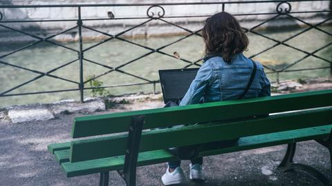 Eine junge Frau sitzt auf einer Bank und schaut in ihren Laptop.