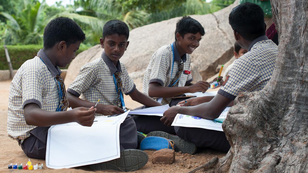 Indische Schulkinder sitzen am in Mahabalipuram (Indien) in einem Park.