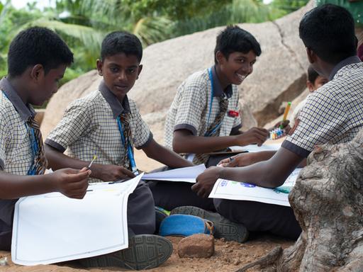 Schulkinder sitzen in Mahabalipuram (Indien) in einem Park.