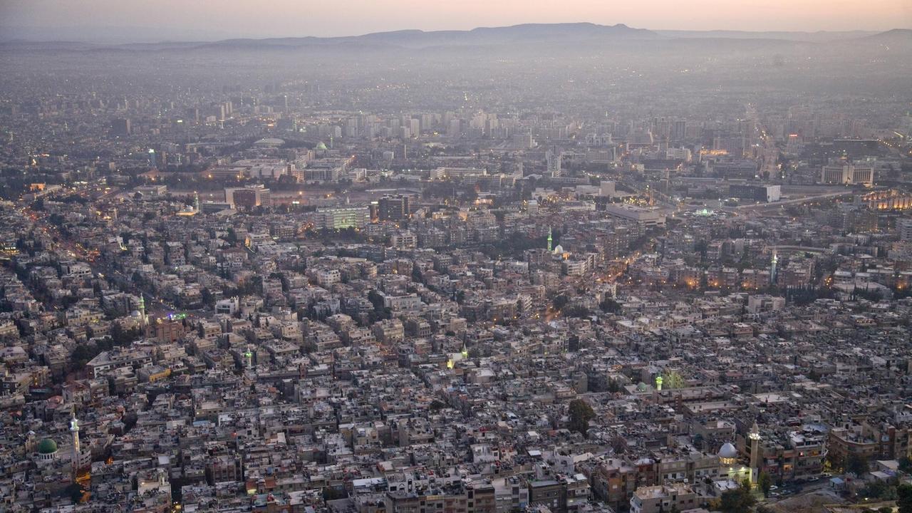 Blick über die Stadtkulisse von Damaskus bei vorangeschrittenem Sonnenuntergang.