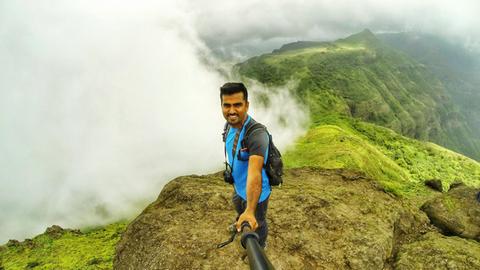 Ein junger Mann steht am rande eines Berges, um ein optimales Selfie machen zu könne.