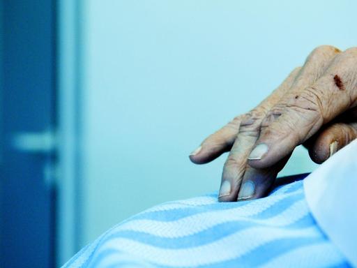 Zu sehen ist die Hand eines alten Menschen auf einer Bettdecke