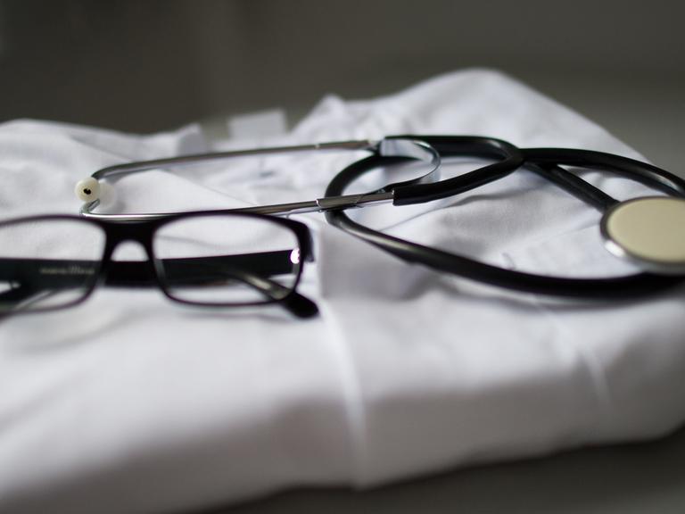 Ein Stethoskop und eine Brille liegen auf einem Arztkittel.