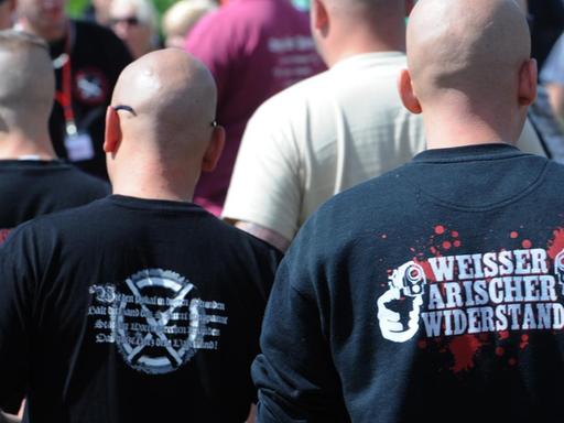 Das Bild zeigt Männer mit kahlgeschorenen Köpfe und schwarzen T-Shirts. Auf einem steht: Weißer, arischer Widerstand.