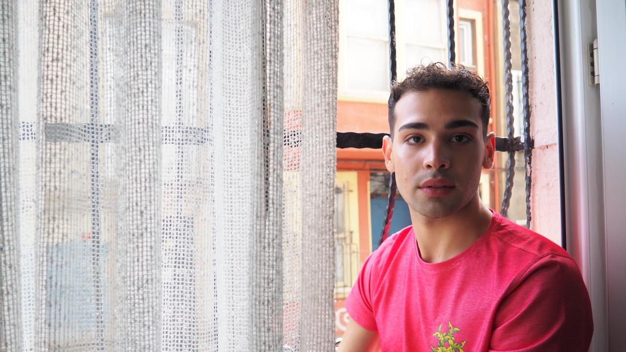 Ein junger Mann sitzt in einem pink T-Shirt am Fenster. Ein junger Mann sitzt in einem pink T-Shirt am Fenster.