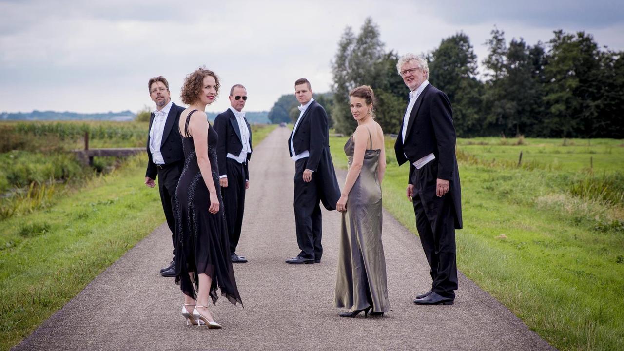 Auf einem Feldweg steht das Ensemble im Kreis und schaut in die Kamera. Die vier Männer tragen Konzertfräcke, die beiden Frauen davor lange, ärmellose Abendkleider . Auf einem Feldweg steht das Ensemble im Kreis und schaut in die Kamera. Die vier Männer tragen Konzertfräcke, die beiden Frauen davor lange, ärmellose Abendkleider .
