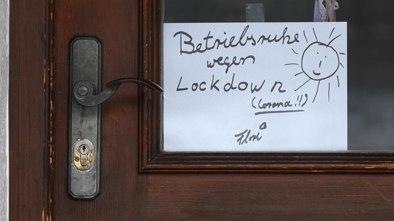 Auf einem handgeschriebenen Schild in einer Tür steht "Betriebsruhe wegen Lockdown", verziert mit einer gemalten Sonne Auf einem handgeschriebenen Schild in einer Tür steht "Betriebsruhe wegen Lockdown", verziert mit einer gemalten Sonne