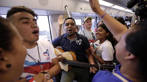 Menschen singen in einem U-Bahn-Abteil, ein Mann spielt Gitarre.