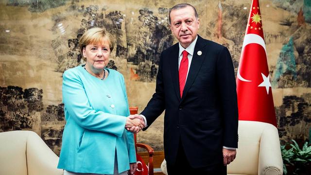 Merkel und Erdogan schauen in die Kamera und schütteln sich die Hände
