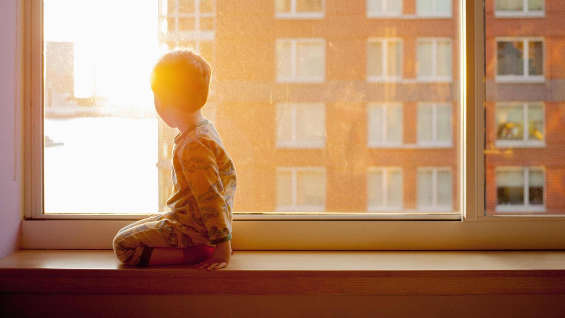Ein Kind kniet auf einer Fensterbank und schaut aus dem Fenster. (Symbolbild) Ein Kind kniet auf einer Fensterbank und schaut aus dem Fenster. (Symbolbild)