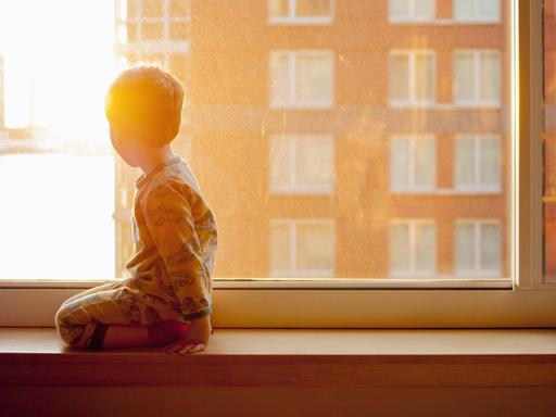 Ein Kind kniet auf einer Fensterbank und schaut aus dem Fenster. (Symbolbild)