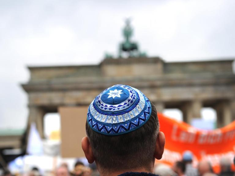 Ein Teilnehmer einer Kundgebung steht vor dem Brandenburger Tor. Er trägt eine Kippa.
